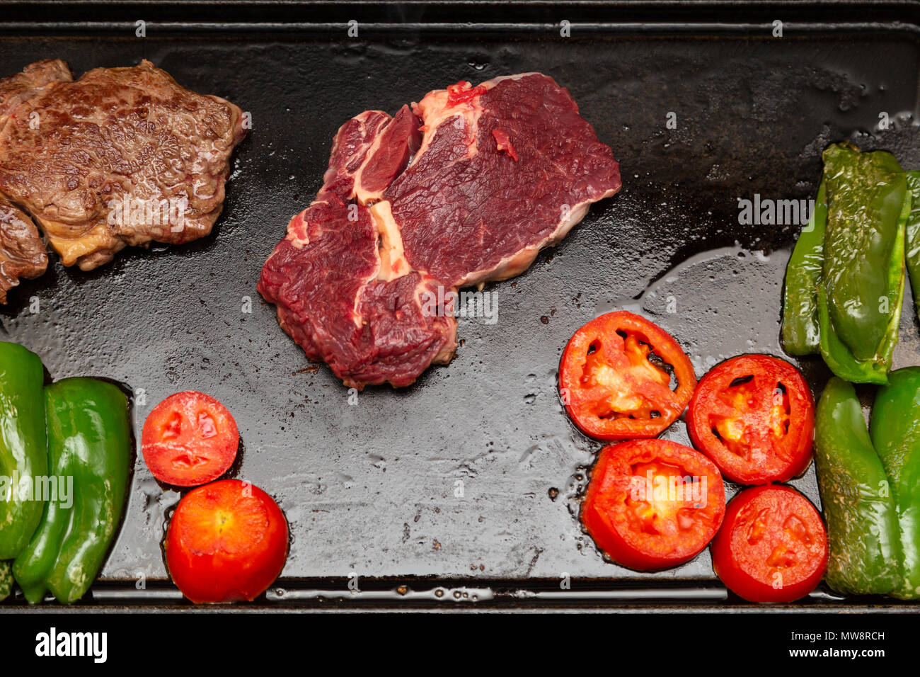 Rib Eye Steak (spanisch: Bife Ancho) roh und gegrillt, Tomaten und grüne Paprika auf rechteckiger Gusseisen flache Pfanne, flach legen Stockfoto