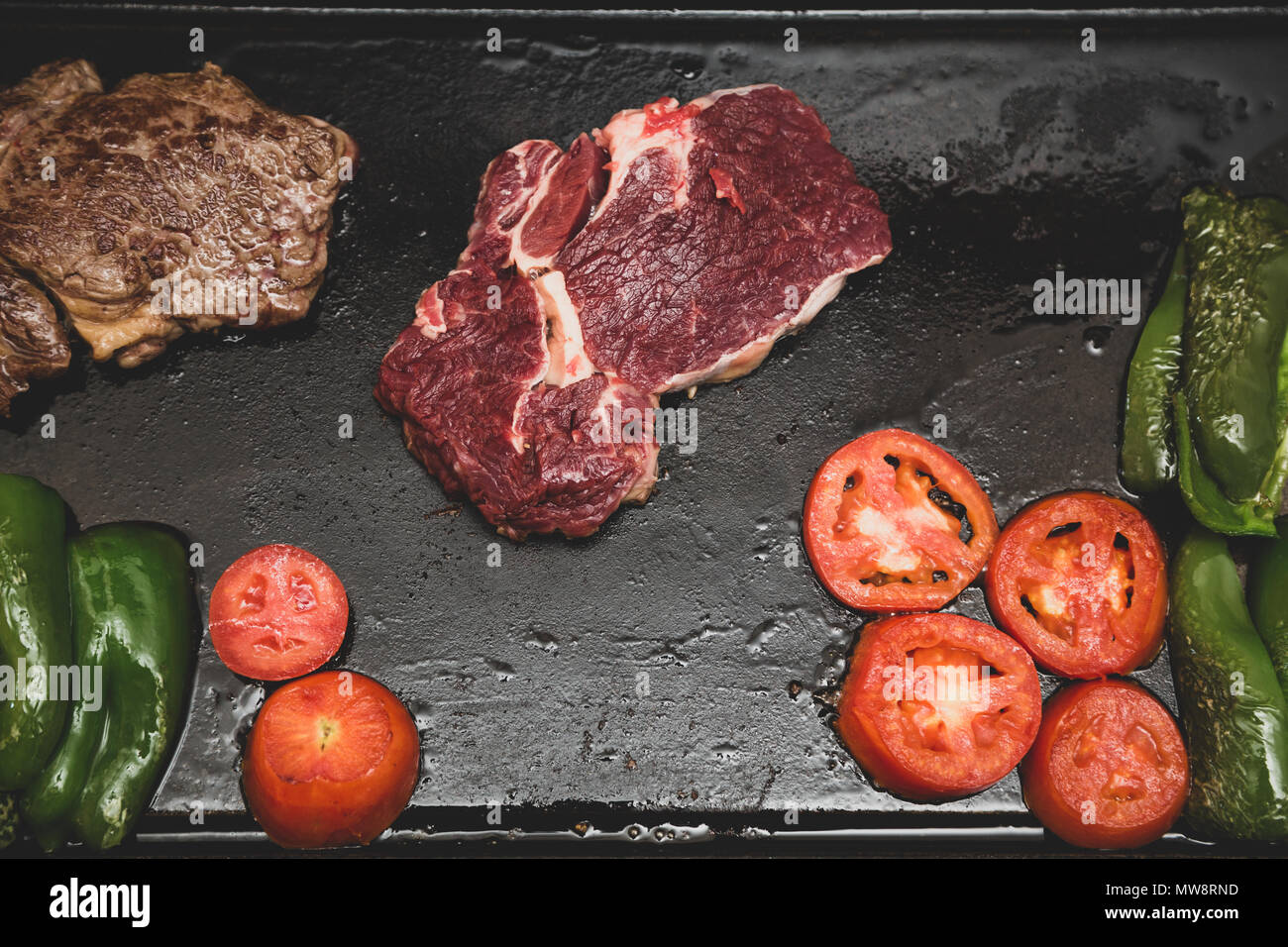 Rib Eye Steak (spanisch: Bife Ancho) roh und gegrillt, Tomaten und grüne Paprika auf rechteckiger Gusseisen flache Pfanne, vintage getönte, flach legen Stockfoto