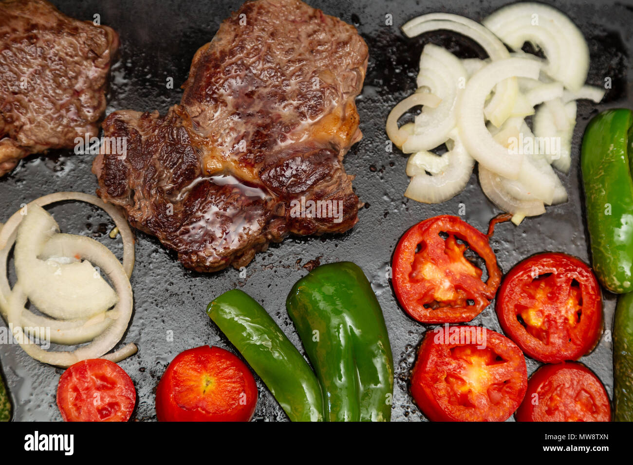 Rib Eye Steak (spanisch: Bife Ancho), Zwiebeln, Tomaten und Paprika auf rechteckigem Gusseisen flache Pfanne gegrillt, flach legen Stockfoto