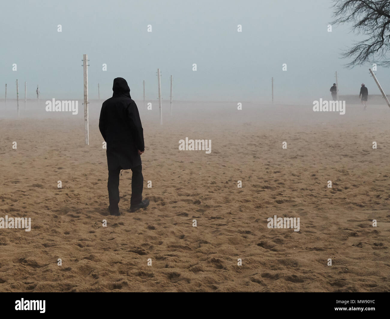 Neblig kalten Frühling Tag entlang der Chicago Lakefront mit Volleyball Pole in Distanz, Silhouette von Mann zu Fuß am Strand im Vordergrund Stockfoto