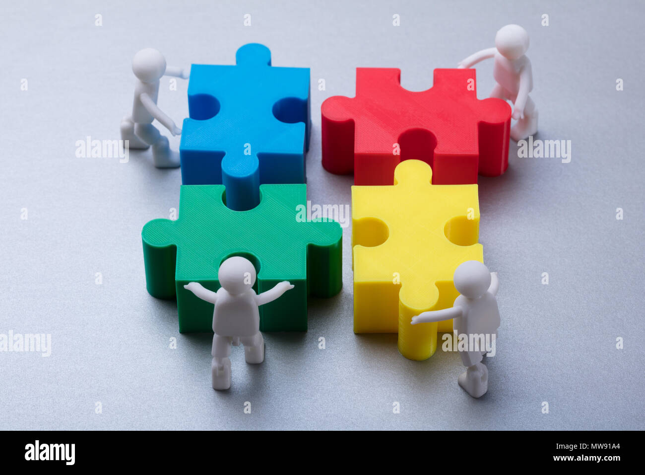 Menschliche Figuren lösen Bunte Puzzle auf grauem Hintergrund Stockfoto