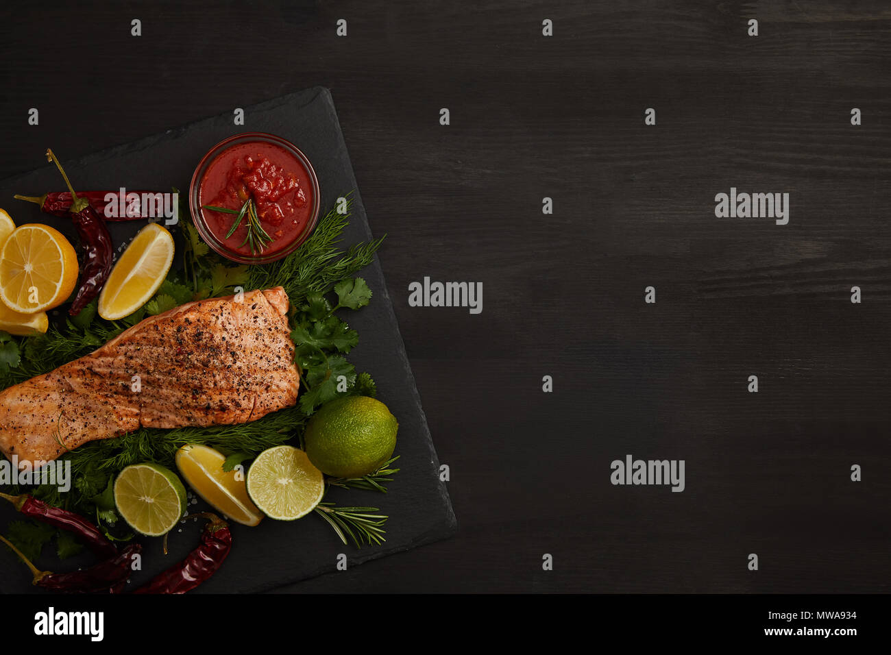 Ansicht von oben gegrilltes Lachssteak, Limette und Zitrone und Soße auf schwarze Oberfläche Stockfoto