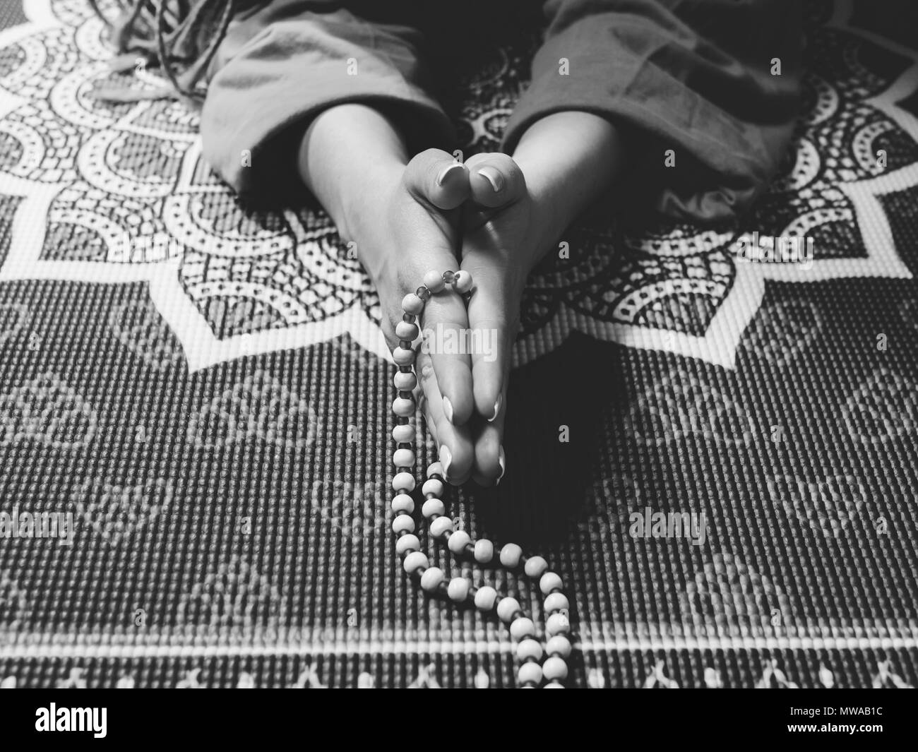 Konzentriert betende Frau mit Holz Rosenkranz auf Yoga Matte mit Mandala. Namaste. Close up Hände. Dankbarkeit Konzept. Schwarz und Weiß Stockfoto