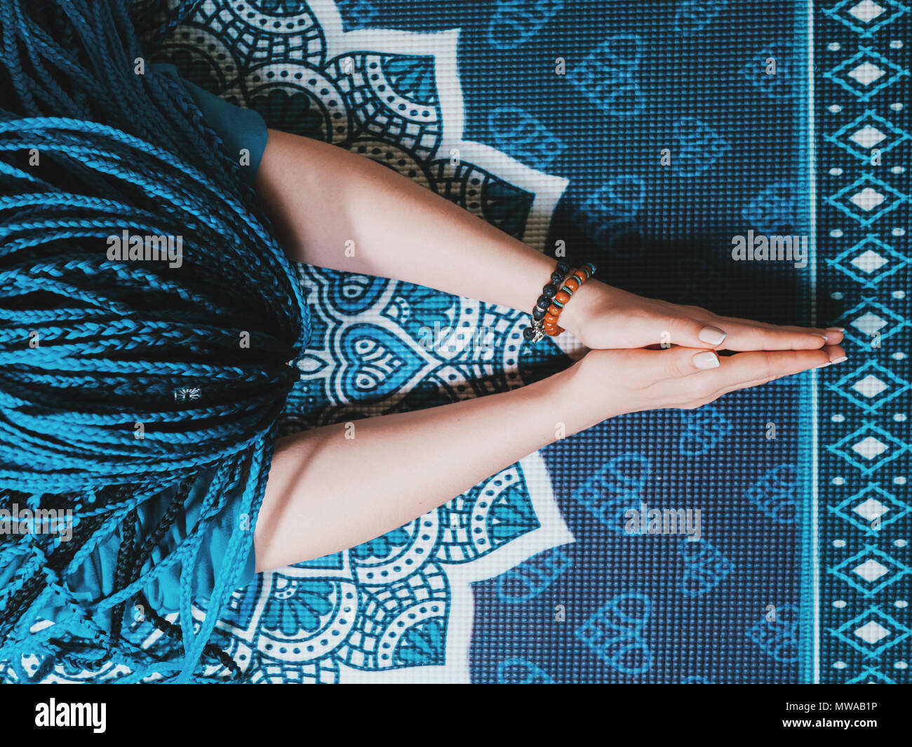 Konzentrierte sich Frau mit blauen afrikanischen Zöpfe beten mit Holz Rosenkranz mala Perlen. Namaste. Nahaufnahme, Hände auf Yoga Matte mit Mandala. Ansicht von oben. Stockfoto