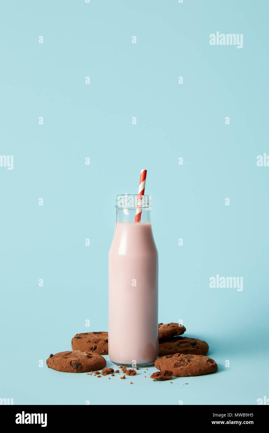 Detailansicht von Erdbeer Milchshake in Flasche mit Strohhalm durch Schokolade Cookies auf blauem Hintergrund umgeben Stockfoto