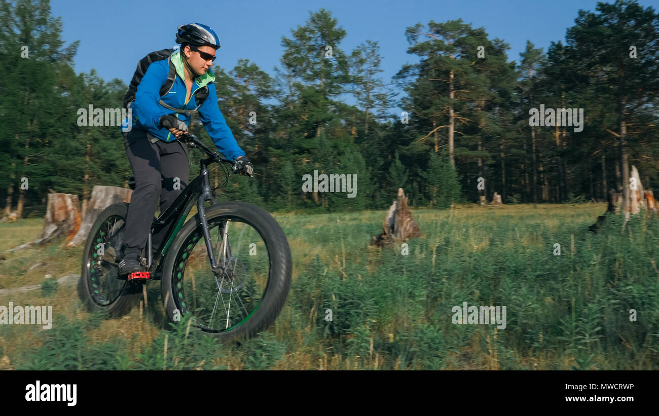 Fat bike auch fatbike oder Fat Tire Bike im Sommer Reiten im Wald. Der Kerl fährt Fahrrad zwischen Bäumen und Stümpfe. Er überwindet einige obstac Stockfoto