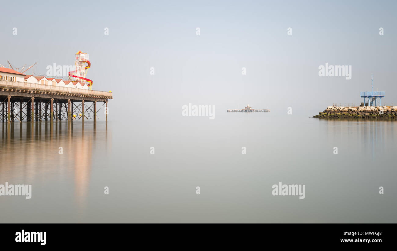 Minimalistischer Kunst Bild der bunten Pier in Gegenüberstellung mit alten verfallenen Pier im Hintergrund Stockfoto