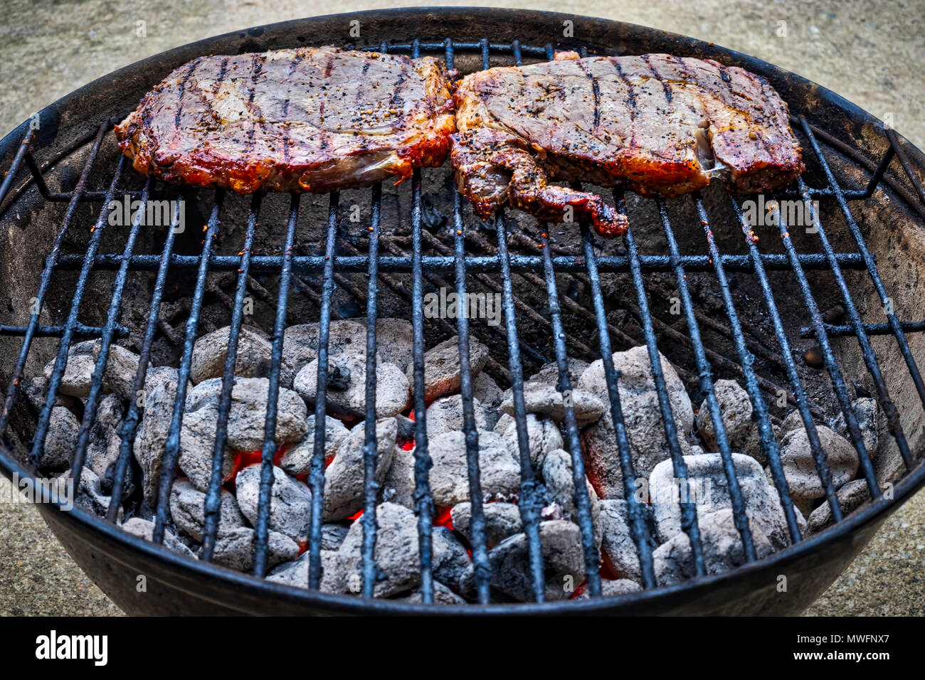 Zwei erfahrene Steaks über Kohlen sitzen auf einem kleinen Grill im Freien. Stockfoto