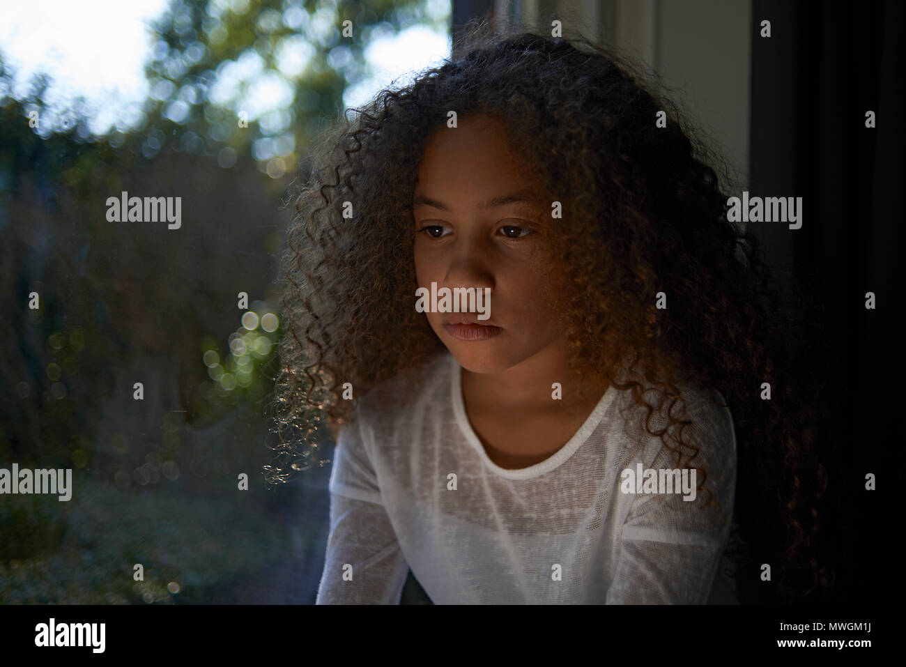 Eine junge Jugendliche gemischt Rennen Mädchen mit grossen lockiges Haar aus dem Fenster ihres Hauses suchen, einsam, traurig und wütend Stockfoto