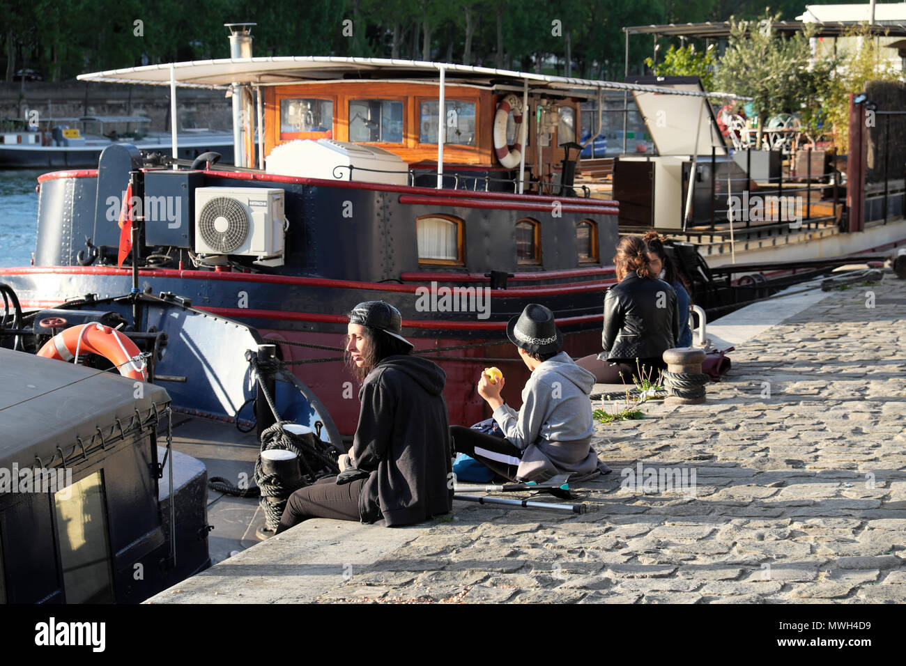 Die Leute sitzen auf einem gepflasterten Quai von Booten auf dem linken Ufer entlang der Seine auf einem Frühling Nachmittag im April Paris, Frankreich KATHY DEWITT Stockfoto