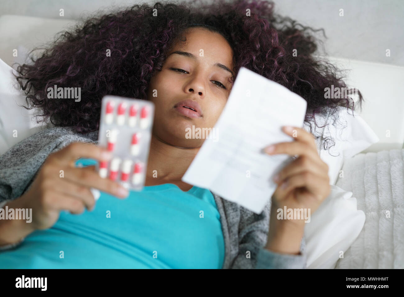 Kranke afrikanische amerikanische Mädchen mit Grippe im Bett zu Hause. Kranke junge schwarze Frau mit kaltem lesen Antibiotika Rezept für Krankheit. Stockfoto