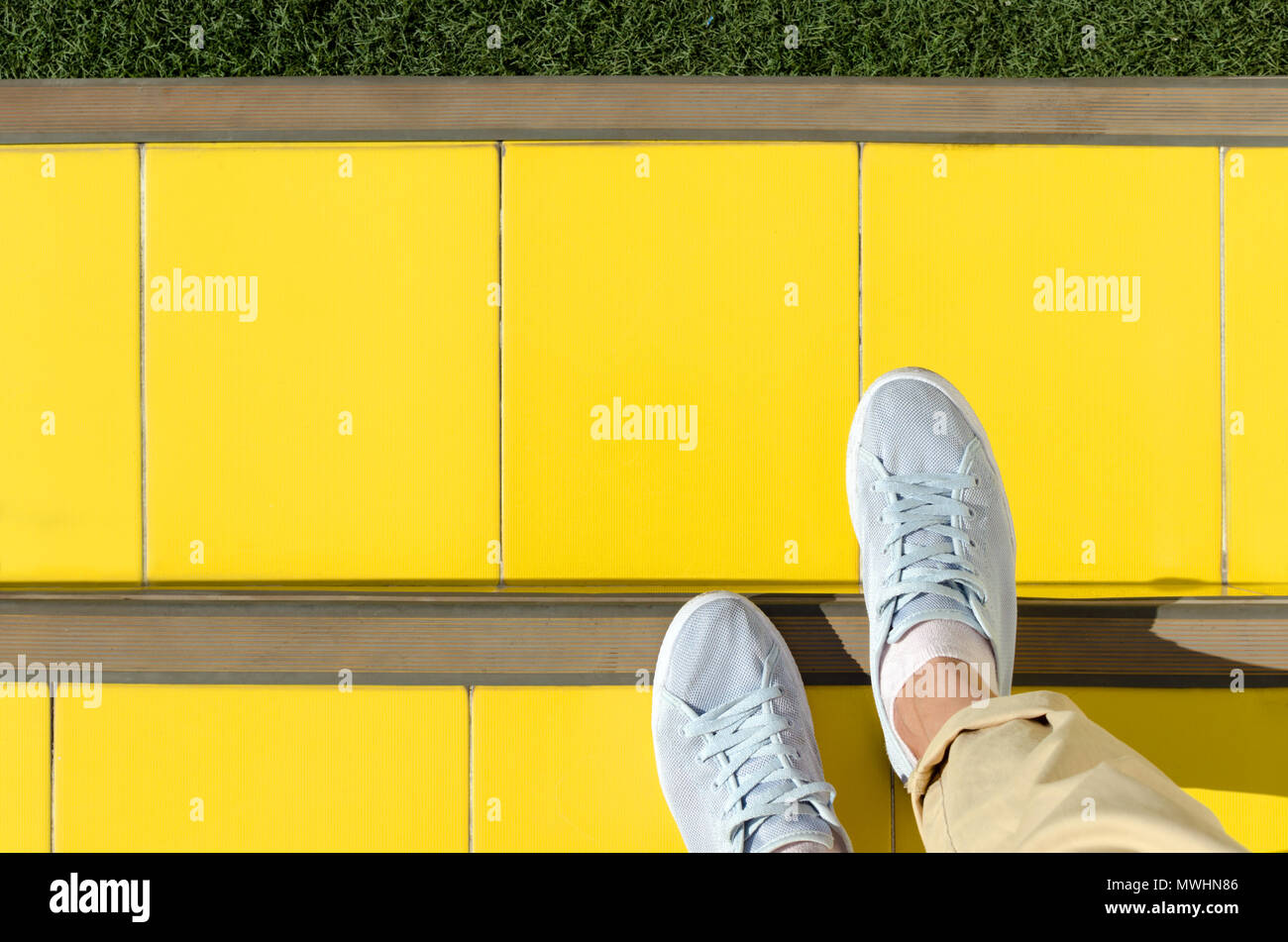 Zusammenfassung Hintergrund - füß im hellblauen Sneakers sind auf Treppen mit gelben Ziegeln gedeckt, vor grünen Rasen. Leere Platz für Text. Stockfoto