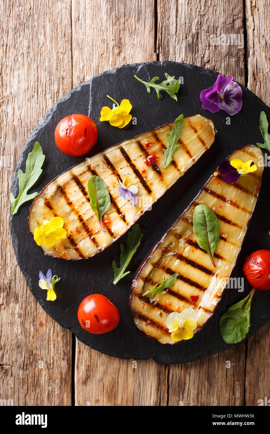 Bio Lebensmittel: gegrillte Auberginen und Tomaten mit Kräuter und essbare Blumen close-up auf den Tisch. Vertikal oben Ansicht von oben Stockfoto