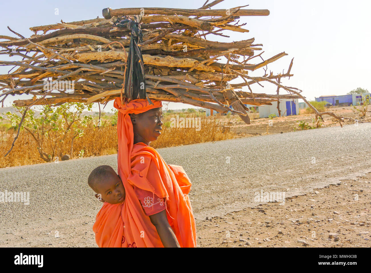 Rashid, Sudan - Februar 5, 2015: Nahaufnahme der sudanesische Frau Baby auf dem Rücken und Holz auf dem Kopf. Bild wurde auf der Straße von Ra genommen Stockfoto