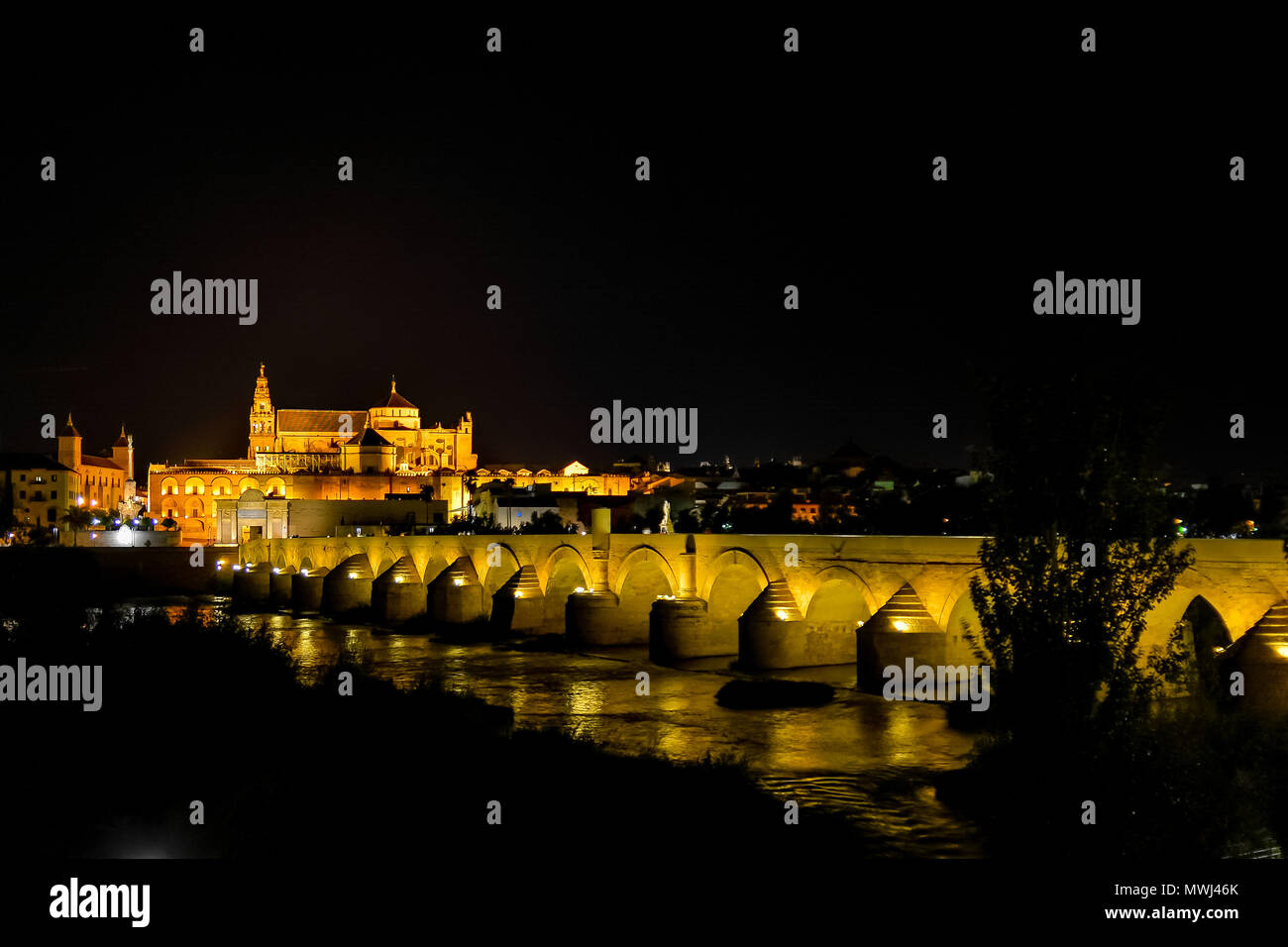 Nächtliche Foto von Cordoba, die Kathedrale und die römische Brücke über den Fluss Guadalquivir, alle von der gelben Lampen und Laternen beleuchteten Stockfoto