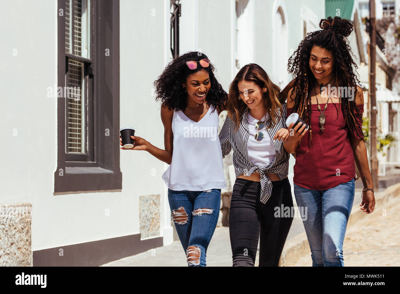 Drei Frauen, die modische Kleidung zu Fuß auf der Straße halten Kaffee Gläser. Stockfoto