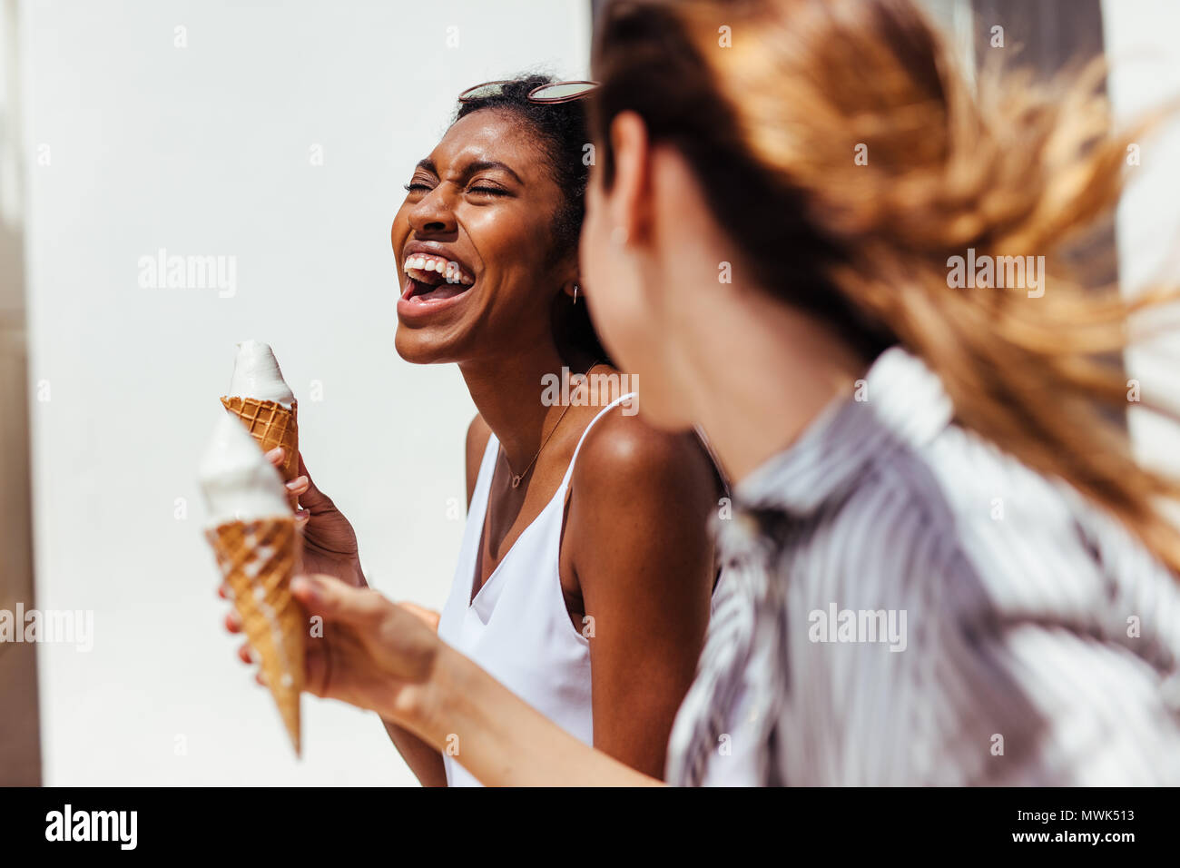 Zwei glückliche suchen Frauen essen Eis Kegel an einem sonnigen Tag im Freien. Stockfoto