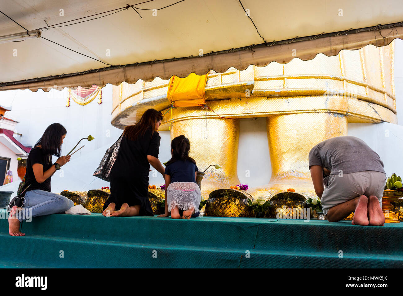 Die Gläubigen vor den Füßen eines Big Standing Buddha im Wat Intharawihan Tempel beten Stockfoto