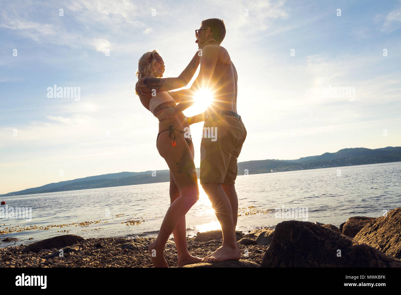 Paar in Liebe einander am Strand gegen Sonne umarmen Stockfoto