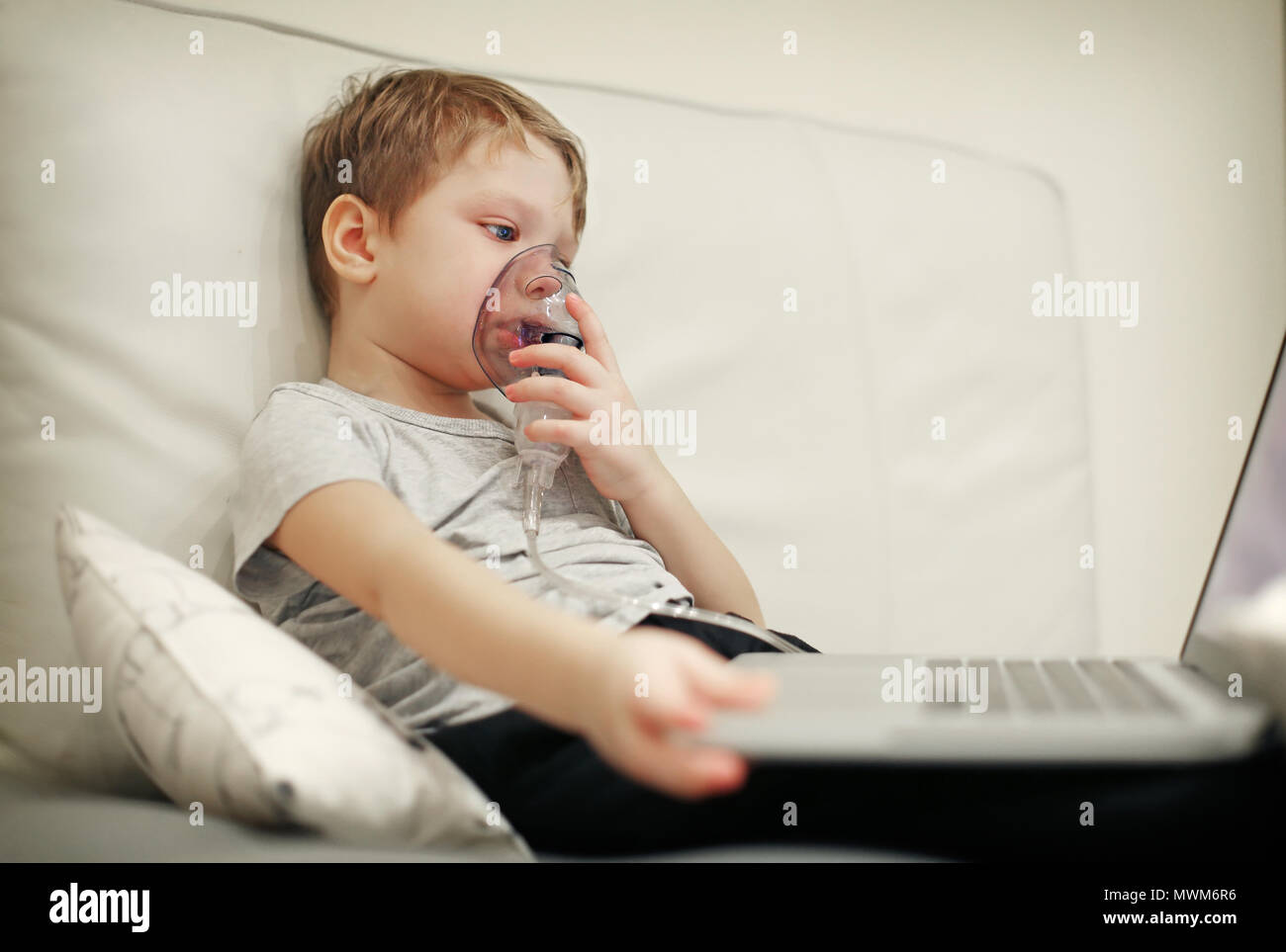 Krankes Kind mit pädiatrischen Vernebler Maske vor dem Laptop. Stockfoto