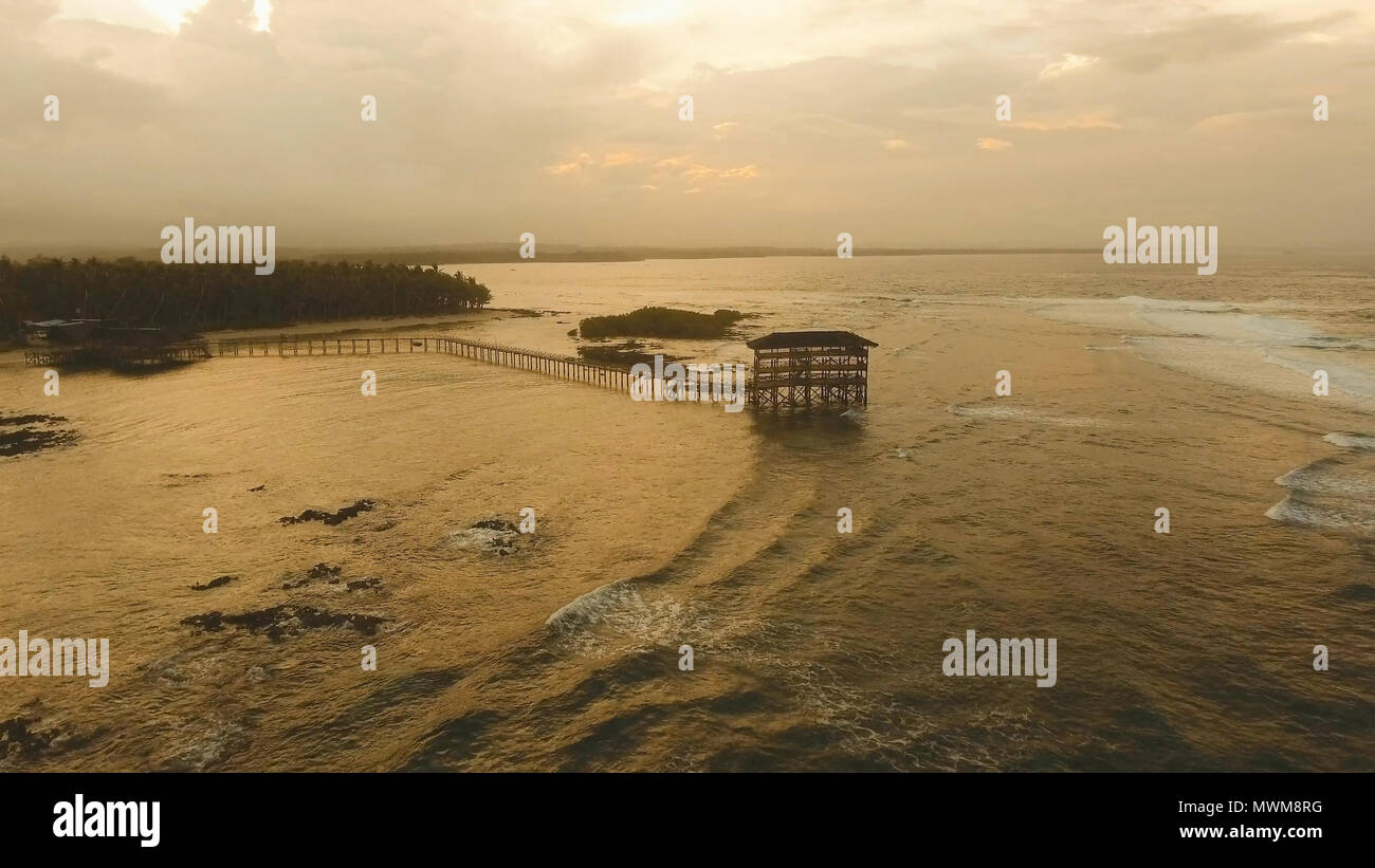 Aussichtspunkt im Meer an Cloud Nine Surf Point bei Sonnenuntergang, Siargao Island, Philippinen. Luftaufnahme angehoben Holzsteg für Surfer das Riff von Siargao Island auf Wolke 9 surf Pause Mindanao. Siargao Inseln berühmte Brandung zerschlagen Wolke 9. Fliegen über dem blauen Meer im azurblauen Lagune. Stockfoto