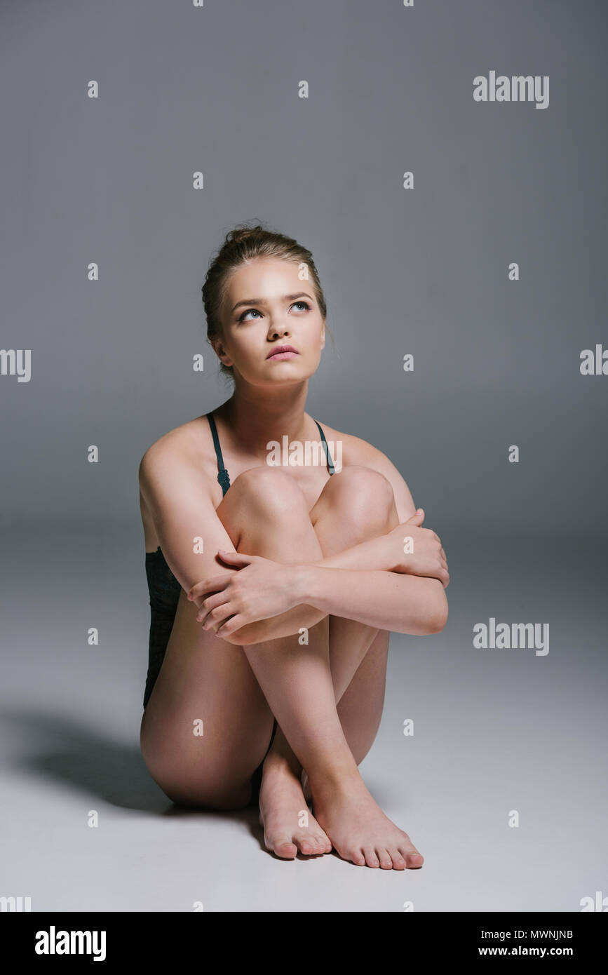 Attraktive nachdenkliche Frau mit schlanken Körper Body tragen und sitzen auf Grau Stockfoto