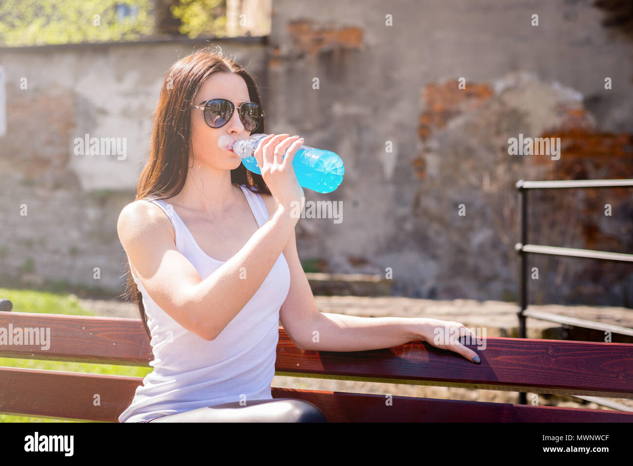 Eine Frau ist Trinkwasser nach der Ausbildung. Eine junge und lächelnde Mädchen trinkt einen Drink Isoton nach körperliche Ermüdung. Weibliche hält eine Flasche mit Blu Stockfoto