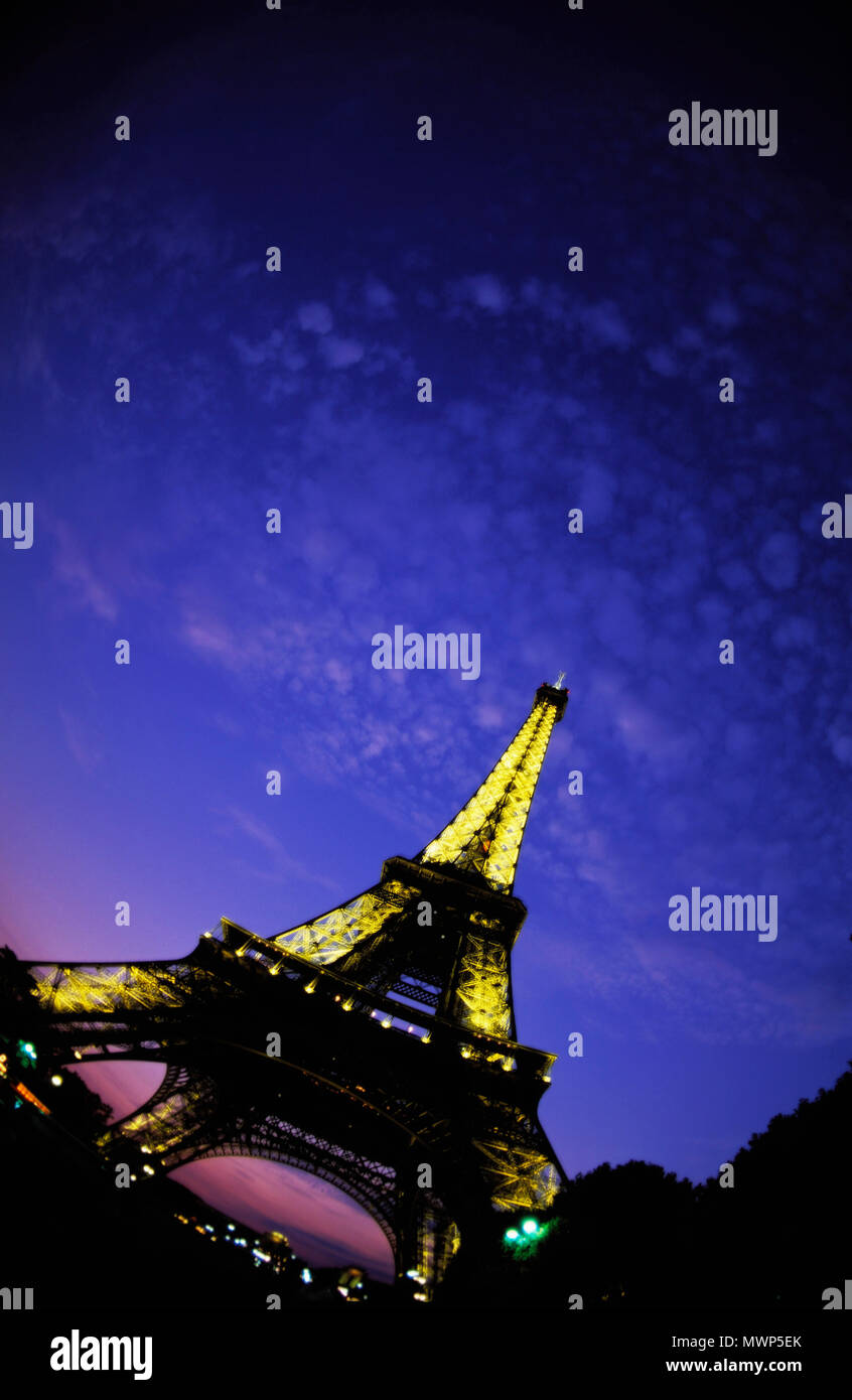Eiffelturm, Nordwesten, Champ de Mars und bis bei Einbruch der Dunkelheit, die Lichter an einem mit Little Fluffy Clouds und Dämmerung glühen, Paris, Frankreich Stockfoto