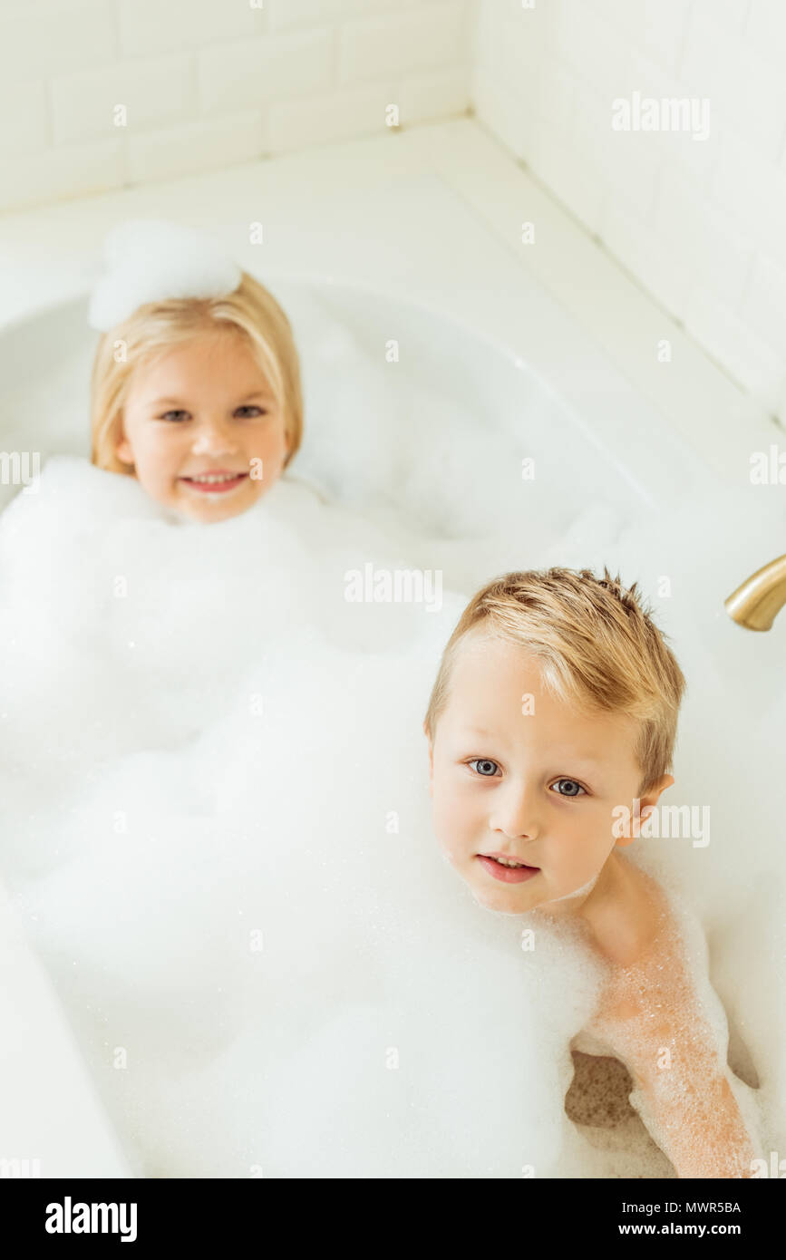 Adorable kleine Kinder lächeln auf die Kamera, während zusammen in der Badewanne sitzen mit Schaumstoff Stockfoto