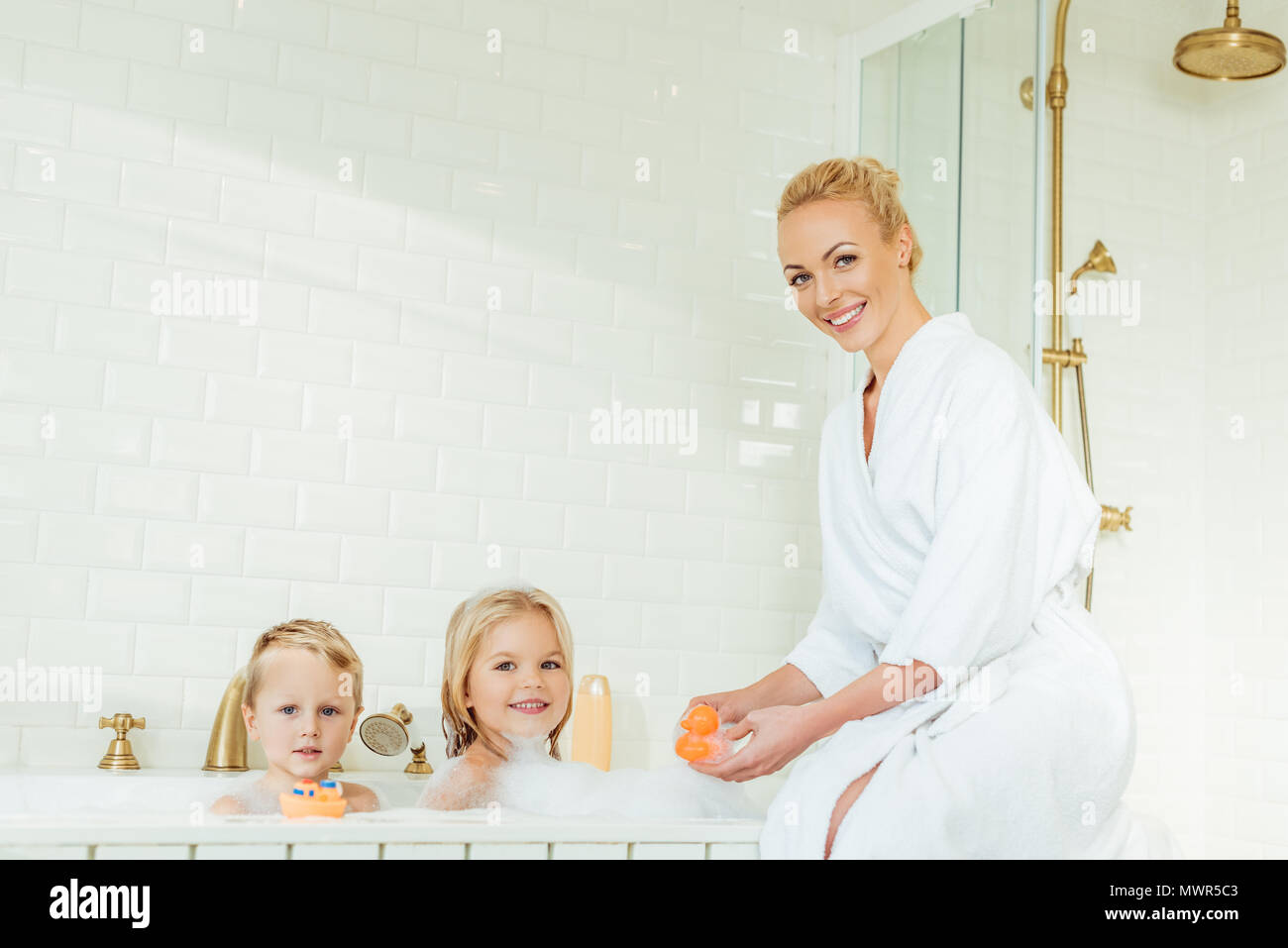 Glückliche Mutter und niedlichen kleinen Kindern ein Lächeln auf die Kamera im Badezimmer Stockfoto