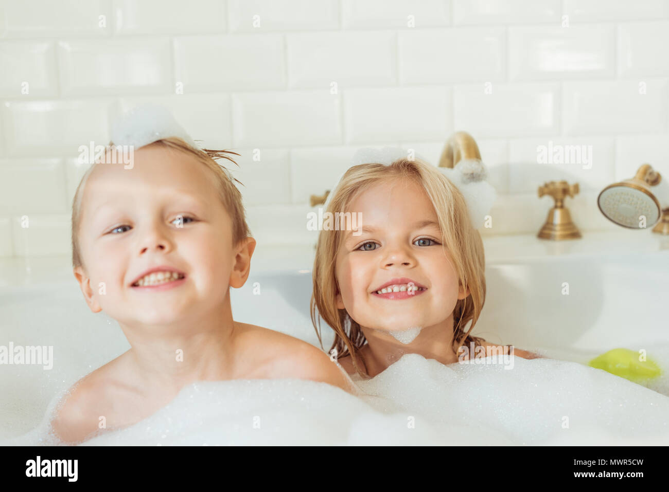Süße kleine Bruder und Schwester lächelnd an Kamera, während sitzen gemeinsam in der Badewanne mit Schaum Stockfoto