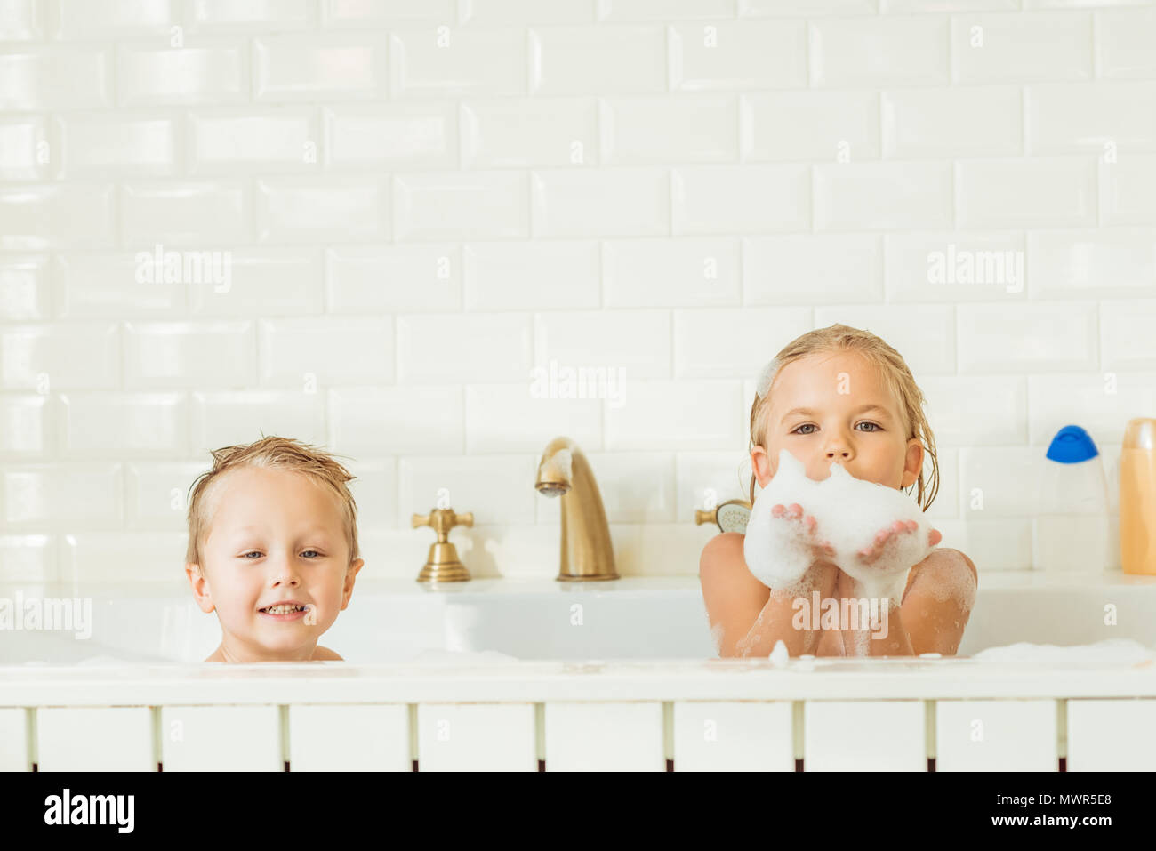 Gerne kleine Kinder sitzen in der Badewanne mit Schaum und lächelnd an Kamera Stockfoto
