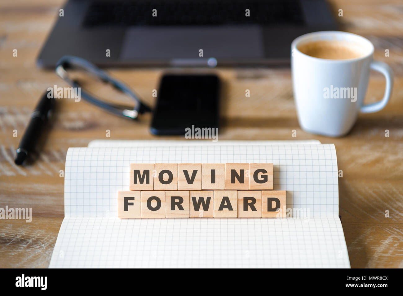 Nahaufnahme auf das Notebook um Holz Tisch Hintergrund, auf Holzblöcken mit Buchstaben, Moving Forward Text konzentrieren. Konzept Bild. Laptop, Brille, Stift ein Stockfoto