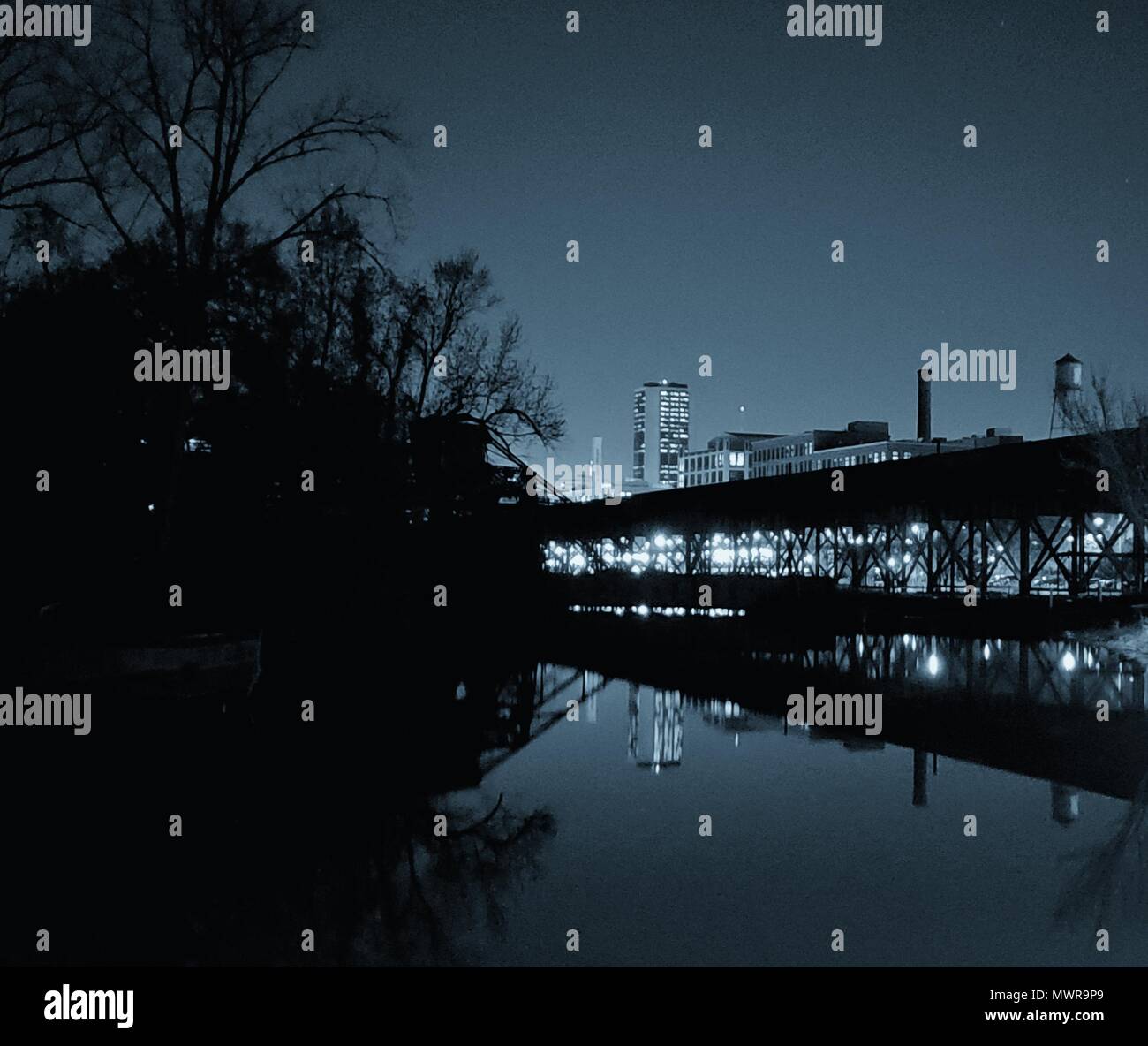 Das Richmond, VA Skyline bei Nacht in ruhigen Kanal Wasser wider. Eine Eisenbahn Brücke führt in die Stadt. Stockfoto