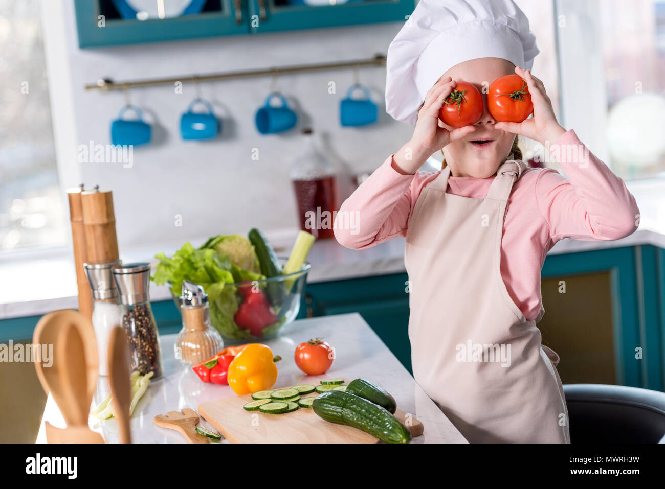 Niedliche Kind in Chef hat und Schürze holding Tomaten beim Kochen in der Küche Stockfoto