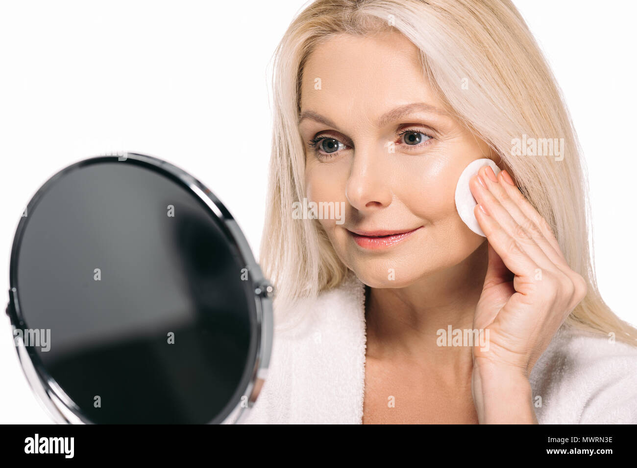 Reife Frau im Spiegel zu betrachten und die Verwendung von kosmetischen Schwamm isoliert auf weißem Stockfoto