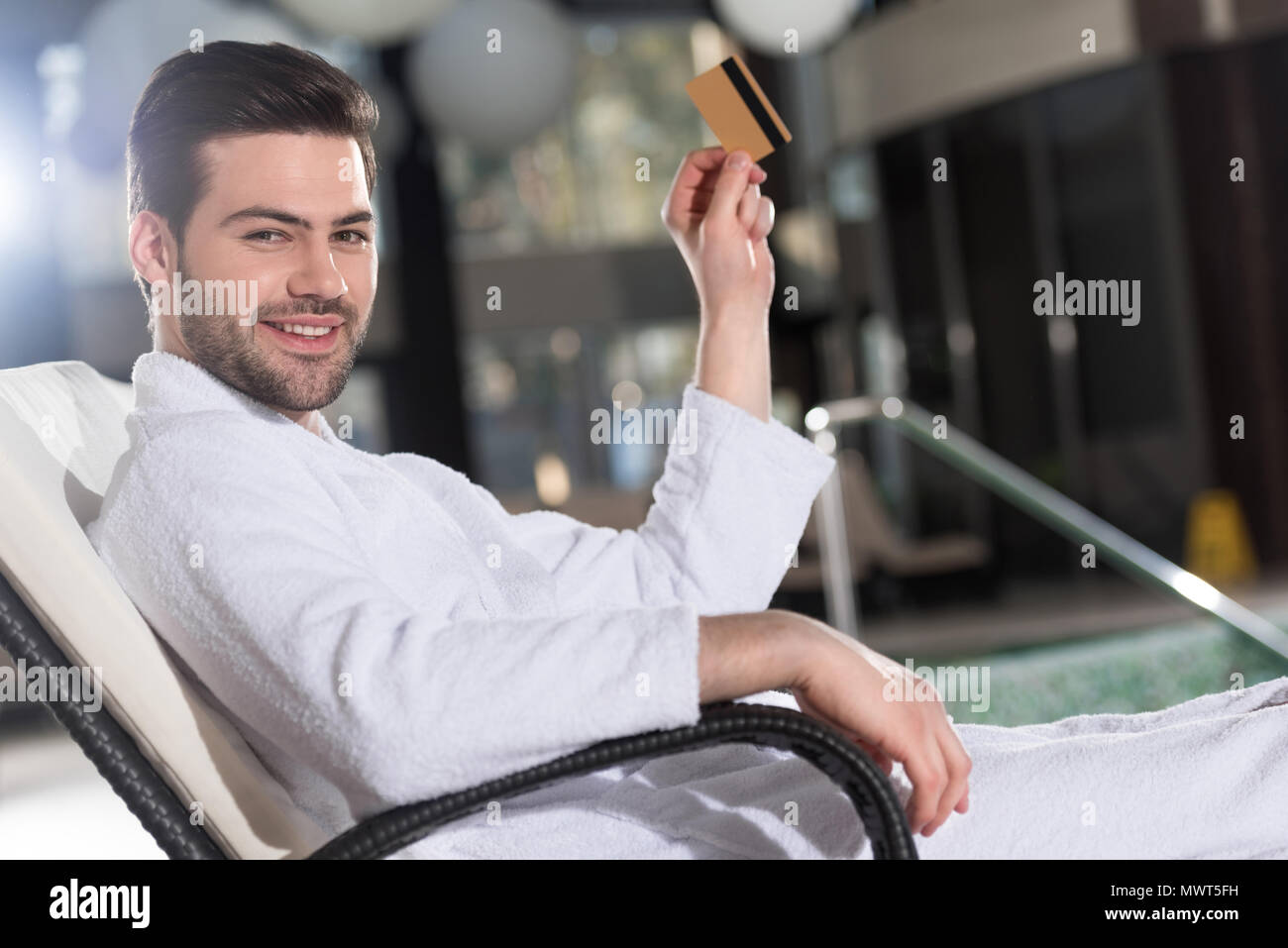 Junger Mann im Bademantel holding Kreditkarte und lächelnd an der Kamera im Spa Center Stockfoto