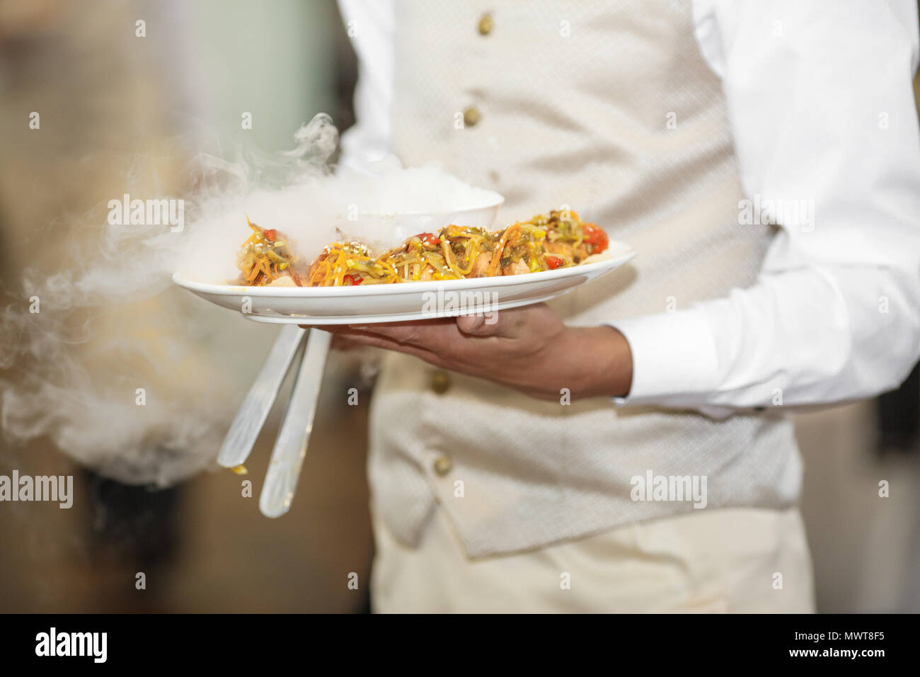 Junger Kellner mit Platte voller leckeren Törtchen bei Party Stockfoto