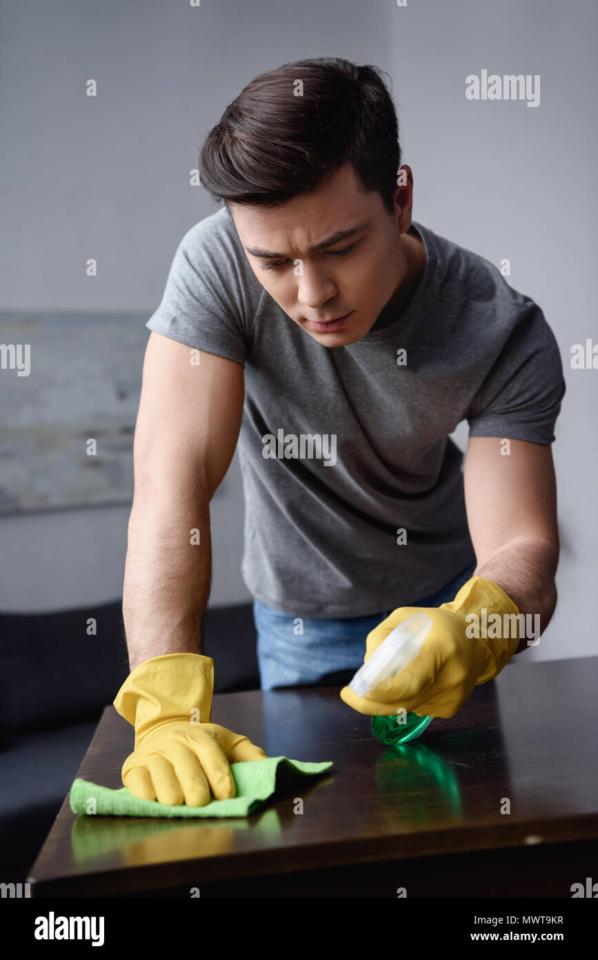 Schöner mann Reinigung Tisch im Wohnzimmer mit Sprühflasche und rag Stockfoto