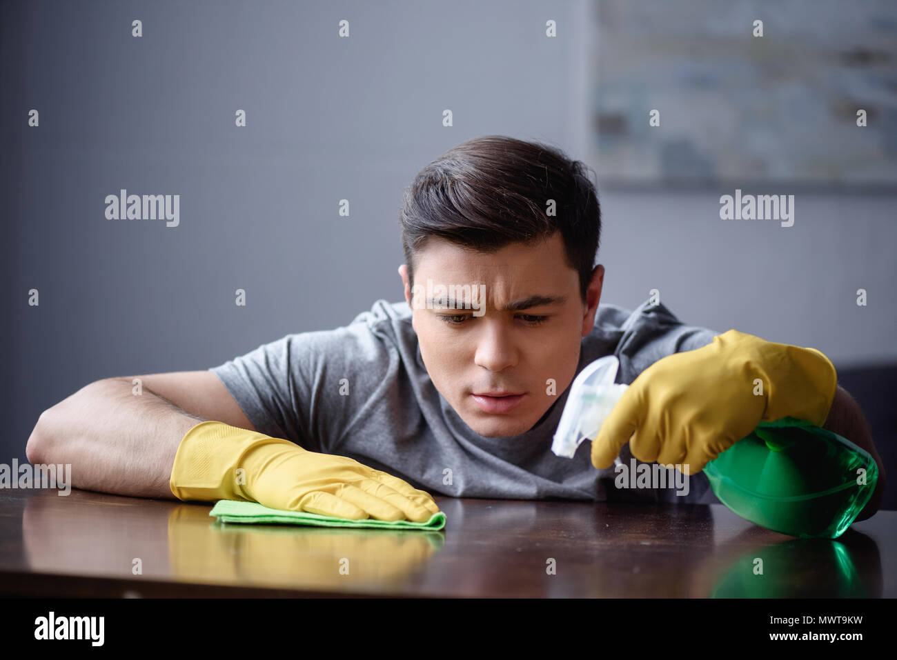 Schöner Mann abstauben Tabelle im Wohnzimmer mit Sprühflasche und rag Stockfoto