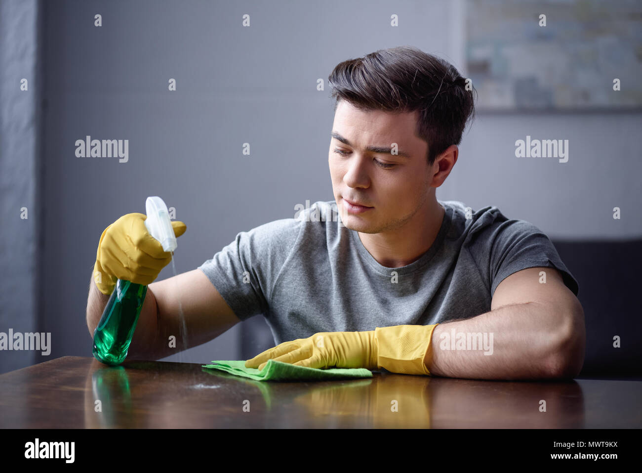 Mann Reinigung Tisch im Wohnzimmer mit Sprühflasche und rag Stockfoto