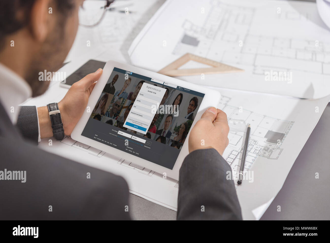 7/8 Schuß von jungen Architekten mit Tablet-PC am Arbeitsplatz Mit Linkedin website auf dem Bildschirm Stockfoto