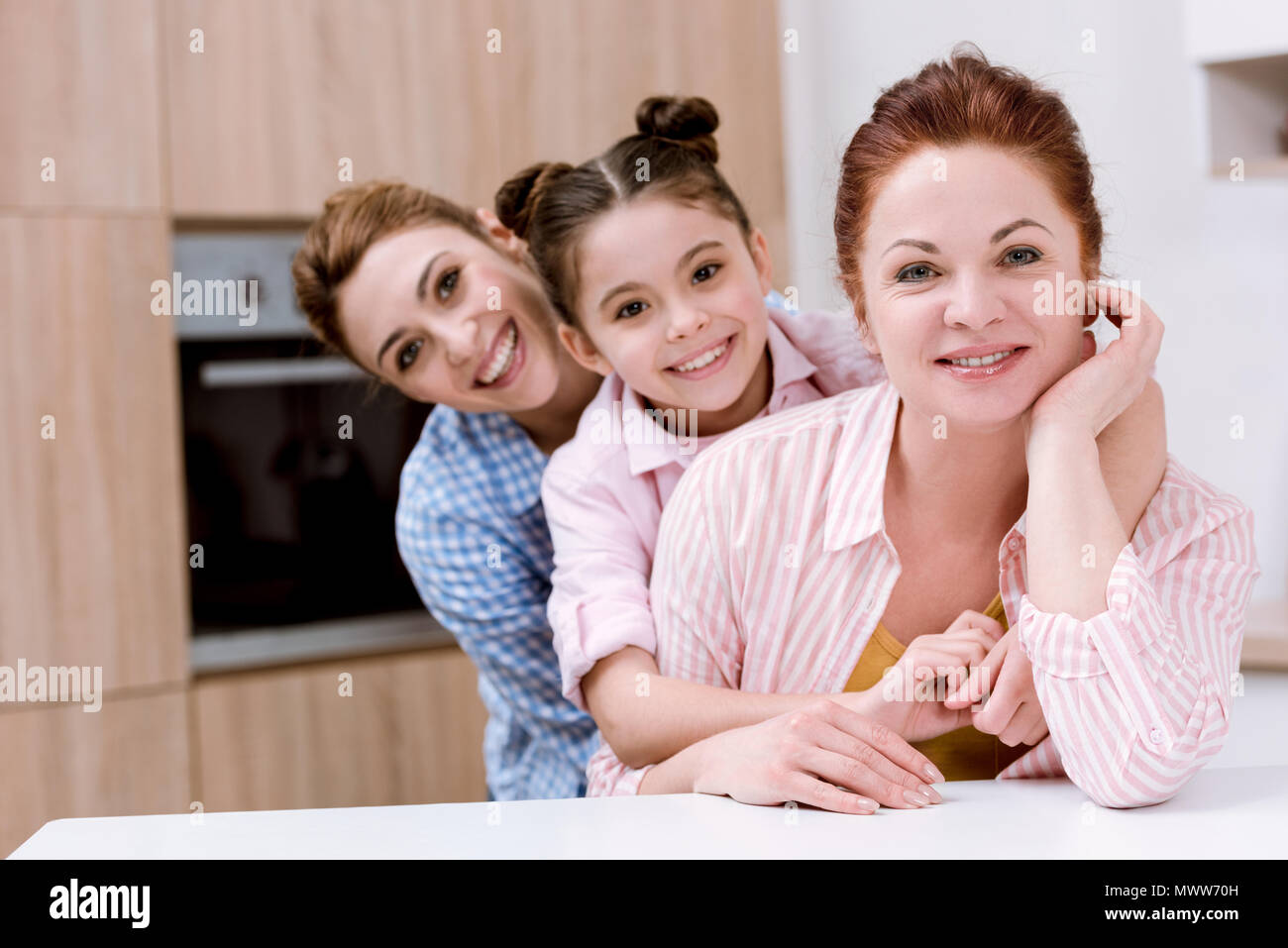 Drei Generationen von gerne schöne Frauen, die in der Zeile zusammen in der Küche und Suchen an Kamera Stockfoto