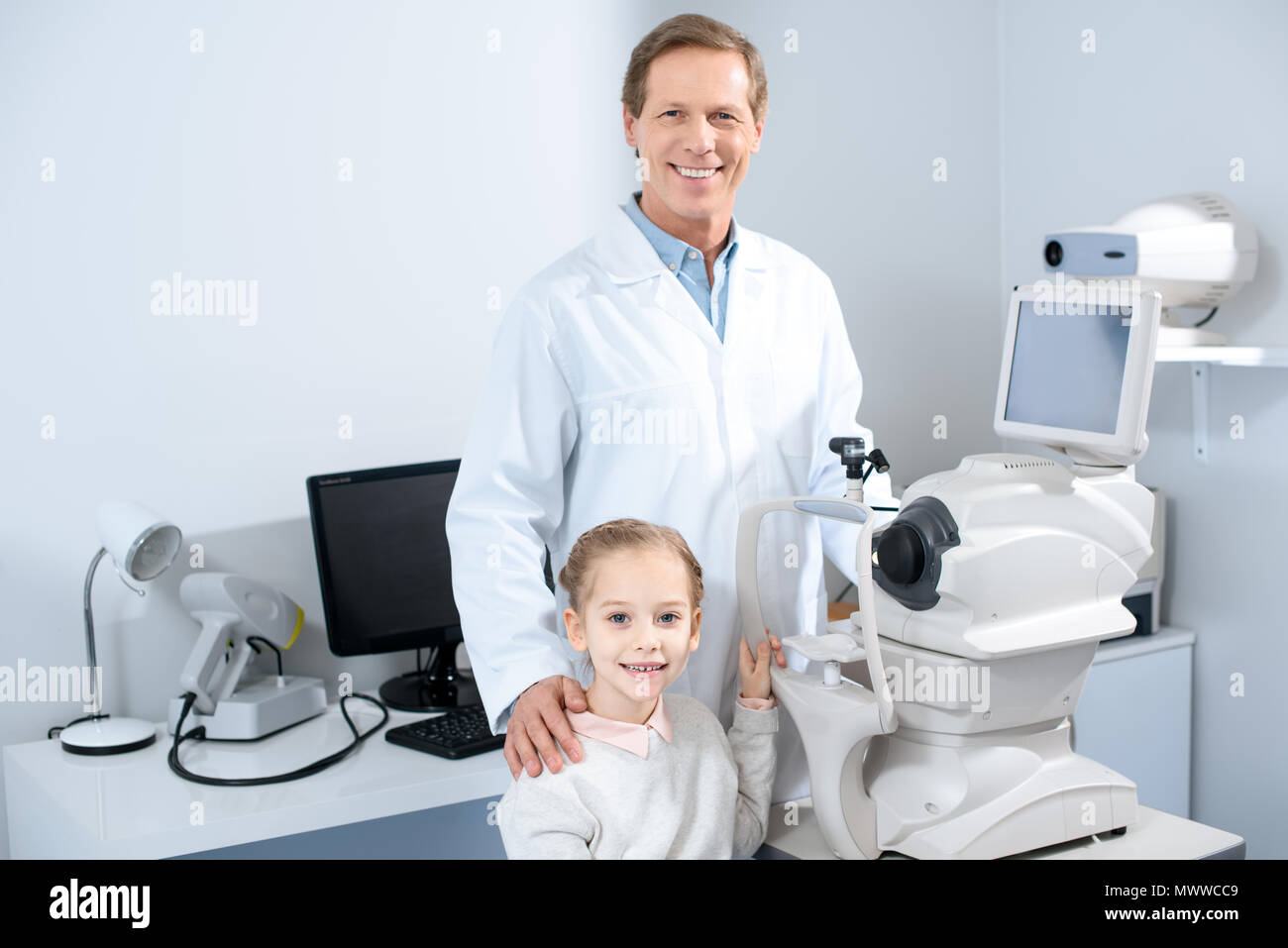 Lächelnd Augenarzt und jugendlicher Kind an der Kamera, in der Klinik auf der Suche Stockfoto
