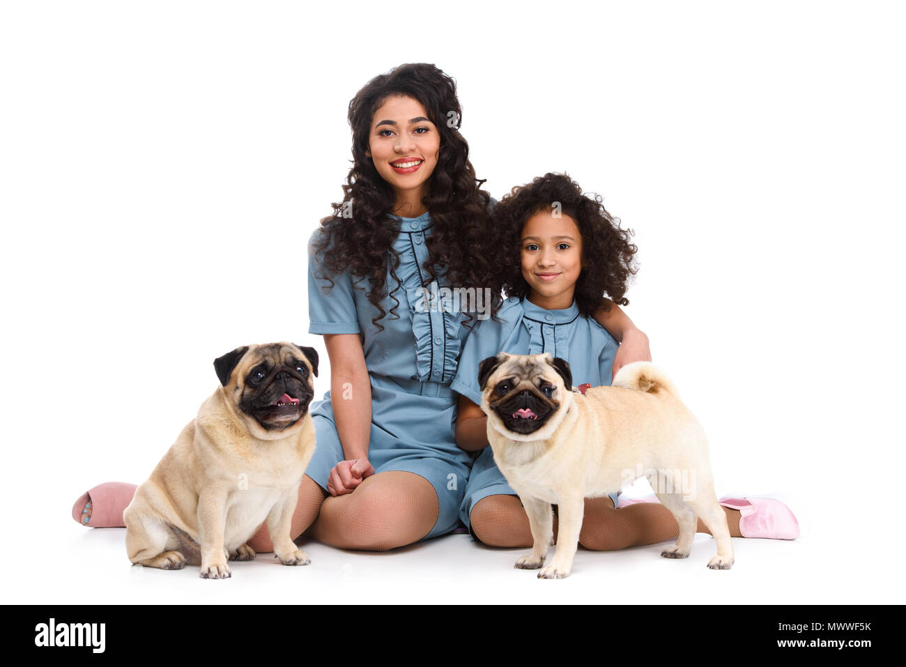 Glückliche junge Mutter und Tochter sitzen auf dem Boden mit zwei möpse isoliert auf weißem Stockfoto