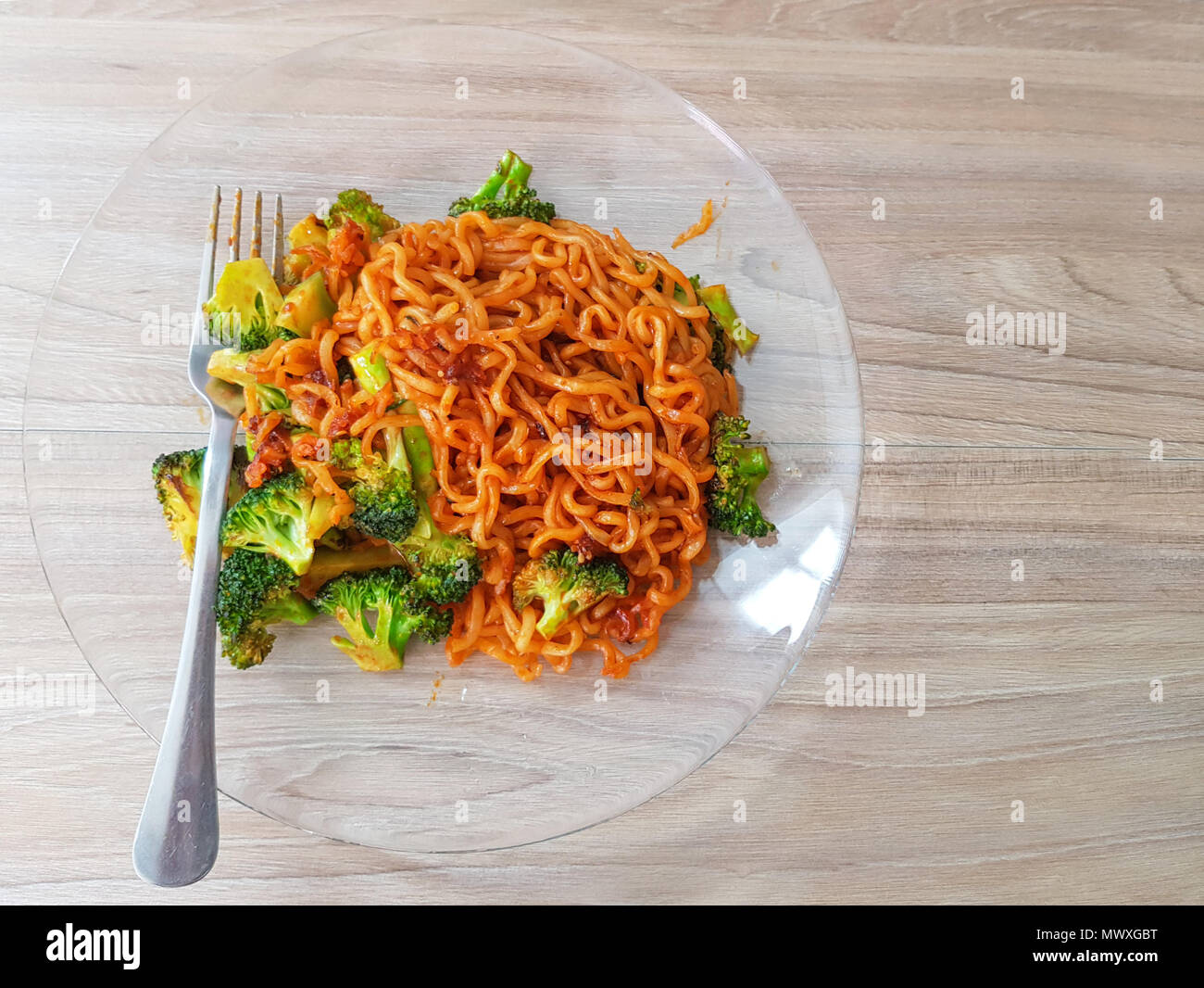 Ansicht von oben. Lecker. Spicy koreanischen instant Nudeln mit grünem Gemüse, auf Teller mit Gabel auf Holz Tisch mit Tageslicht Hintergrund Brokkoli. Stockfoto