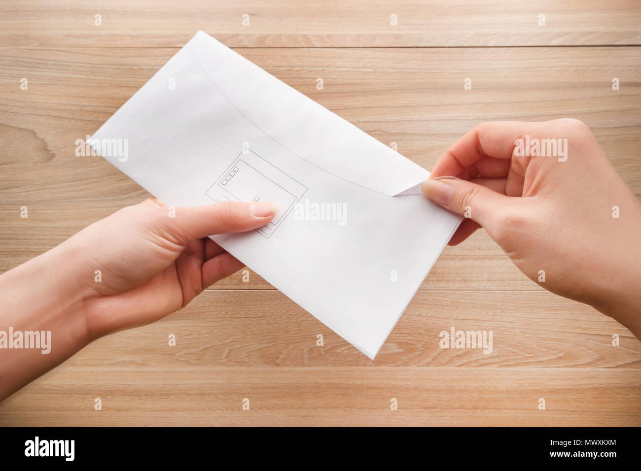 Woman's Hand hält und öffnet einen weißen Umschlag oder Brief Briefumschläge auf einem hölzernen Schreibtisch Draufsicht Hintergrund. Stockfoto