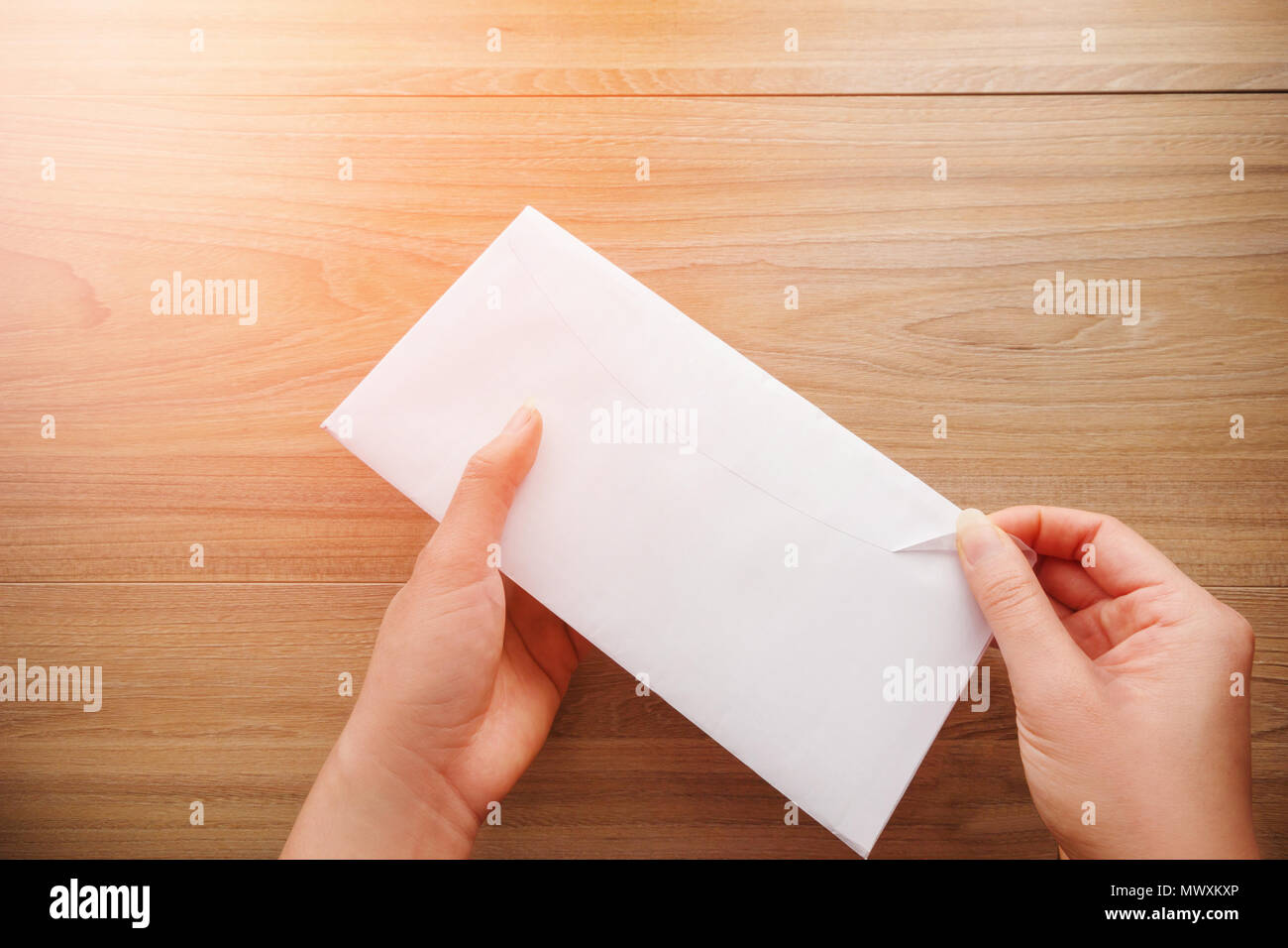 Woman's Hand hält und öffnet einen weißen Umschlag oder Brief Briefumschläge auf einem hölzernen Schreibtisch mit natürlichem Sonnenlicht am Morgen, Ansicht von oben Hintergrund. Stockfoto