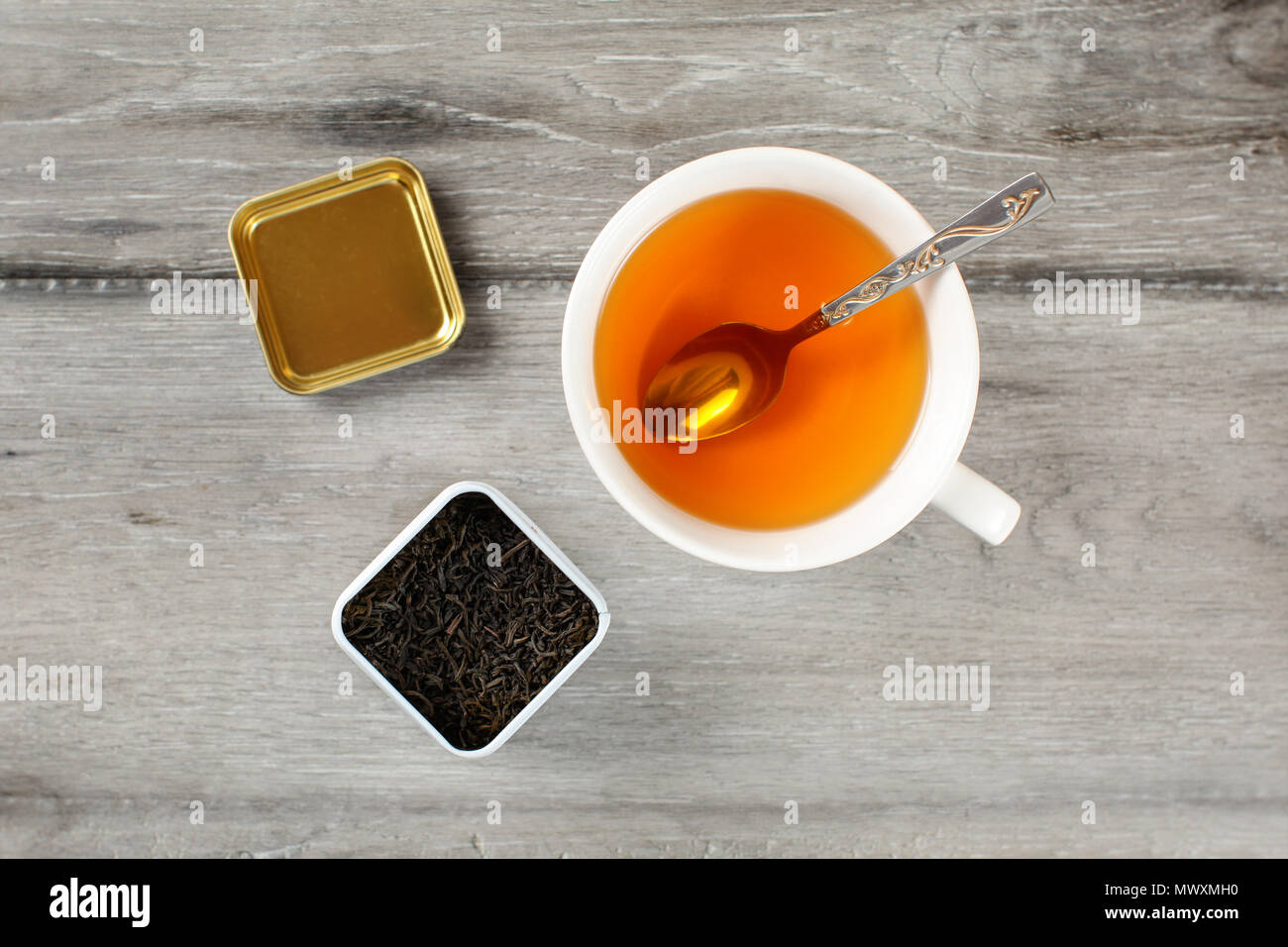 Table Top Blick auf heiße Tasse Kaffee mit Löffel, Gelb und Caddy voll schwarzem getrocknet lose Blätter, auf grau Holz Schreibtisch platziert. Stockfoto