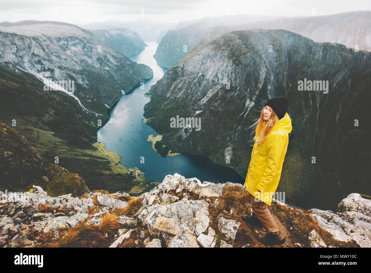 Frau Reisenden auf Klippe alleine stehen Reisen in Norwegen Lifestyle Abenteuer Ferien Antenne fjord view Mädchen tragen gelbe Regenmantel walki Stockfoto